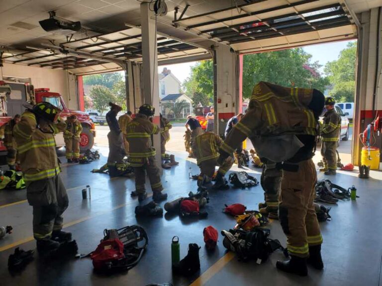 firefighters gathered around practicing putting on and taking off personal protective equipment as part of their training academy