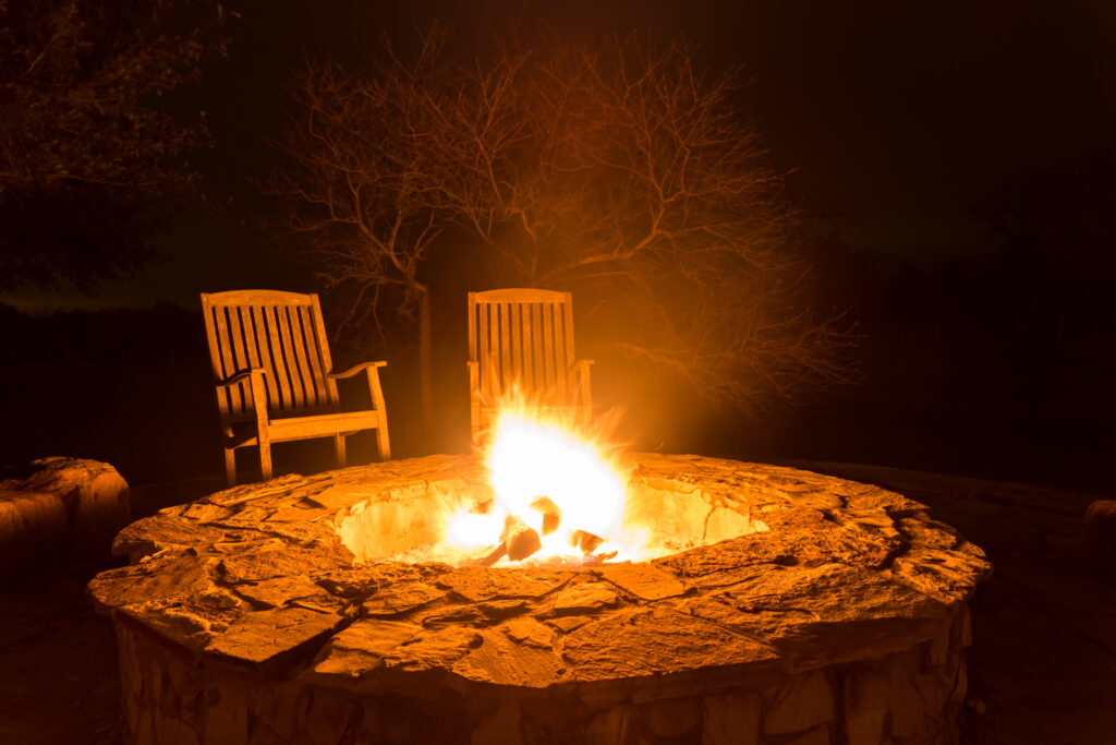 Fire pit aflame with two empty chairs and dark forest